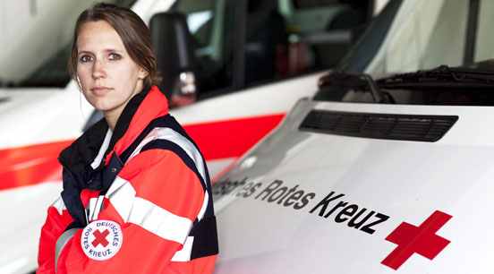 Foto: Eine Rettungssanitäterin lehnt an einem Rettungswagen.