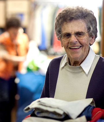 Seniorin trägt lächelnd einen Stapel Kleidung