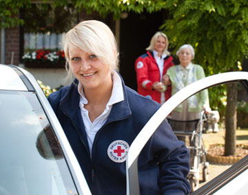 Foto: Eine blonde Pflegekraft steht lächelnd an einem Einsatzwagen.