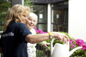 Foto: Pflegekraft hilft Seniorin beim Blumengießen